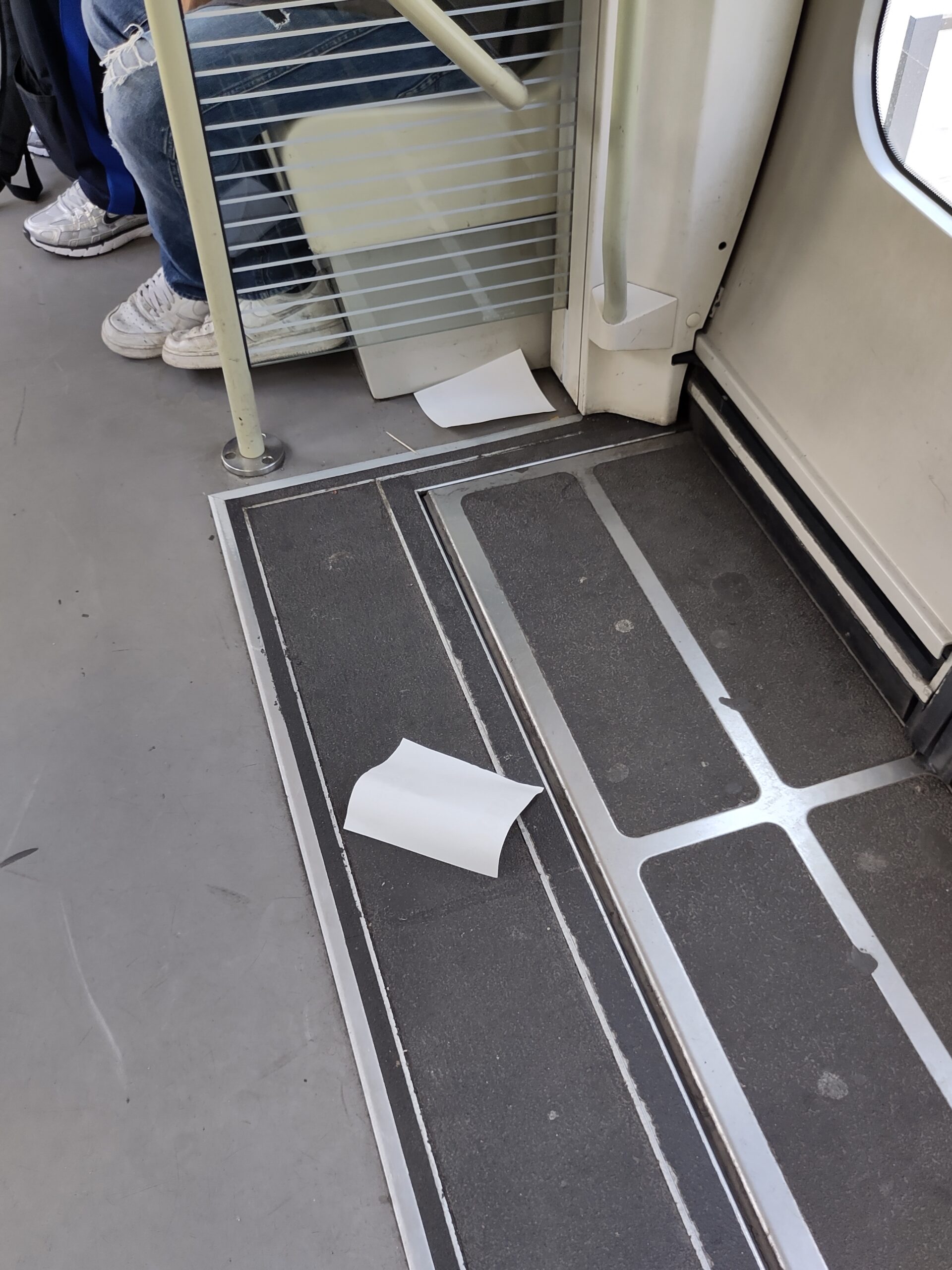 Blick auf den Boden einer Straßenbahn im Bereich einer Tür. Rechteckige Stücke eines Aufklebers liegen auf dem Boden.