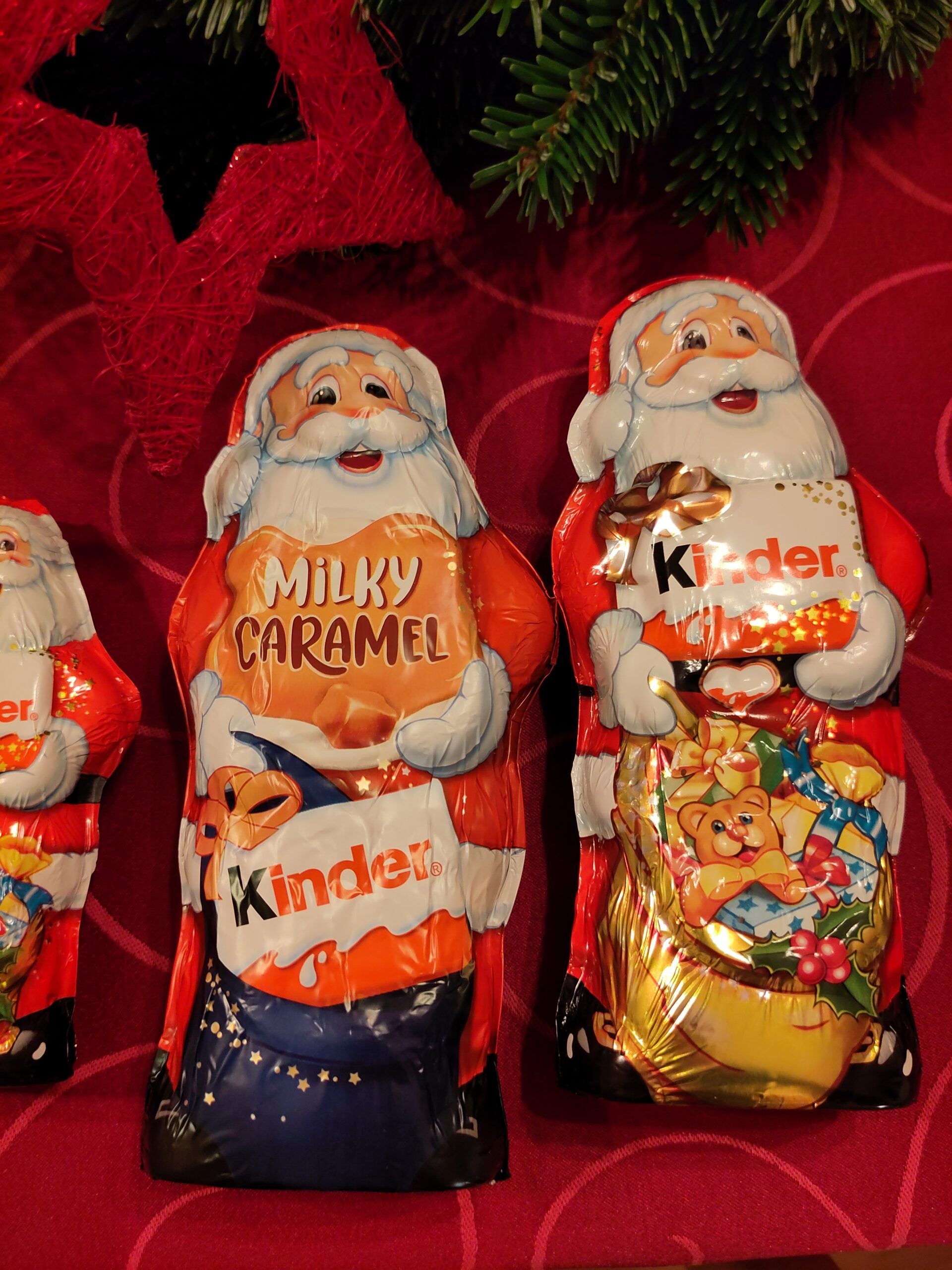 Mehrere Schokoladen-Nikoläuse unterschiedlicher Hersteller und Größe liegen nebeneinander auf einem Tisch. Am oberen Rand sieht man Tannenzeweige und einen roten Stern.